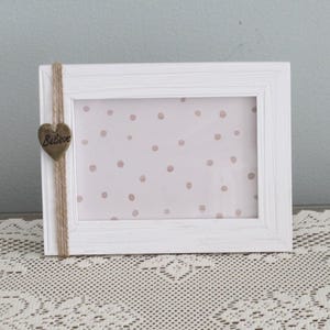 May include: White picture frame with a rustic twine accent and a wooden heart with the word "Believe" inscribed on it. The frame has a pink and white polka dot background.