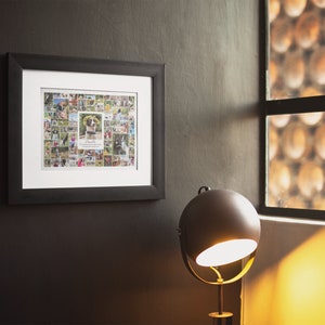May include: A black framed photo collage with a white mount. The collage features a variety of photos of a dog, including close-ups of the dog's face and photos of the dog playing outside. The collage is hanging on a dark grey wall.