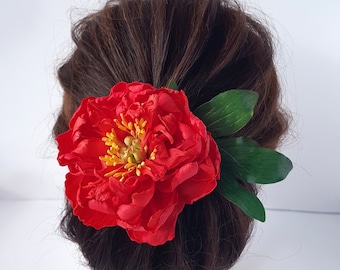 Op de afbeelding: Een rode pioenroos met groene bladeren, gedragen als haaraccessoire.