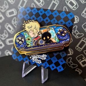 Può includere: Uno spillo in smalto dorato che rappresenta una console per videogiochi blu e viola con un personaggio di un videogioco. Il personaggio è sdraiato con la testa appoggiata sulla console. Lo spillo ha uno sfondo a scacchi e il testo "Chemist Pins".