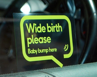 May include: A green and black sticker on a car window that says "Wide birth please Baby bump here" with a smiley face.