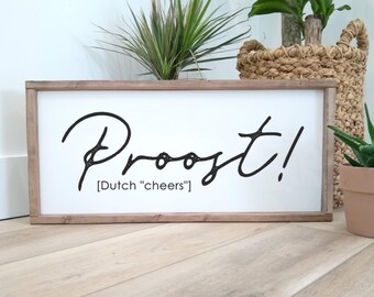 May include: A white wooden sign with the word "Proost!" written in black cursive script. Below the word is the text "[Dutch "cheers"]".