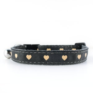 May include: A black cat collar with a silver bell and gold heart pattern.