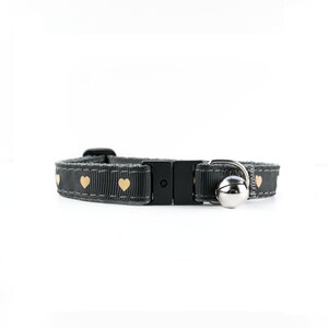 May include: A gray cat collar with a safety breakaway buckle and a small bell. The collar is decorated with gold hearts.