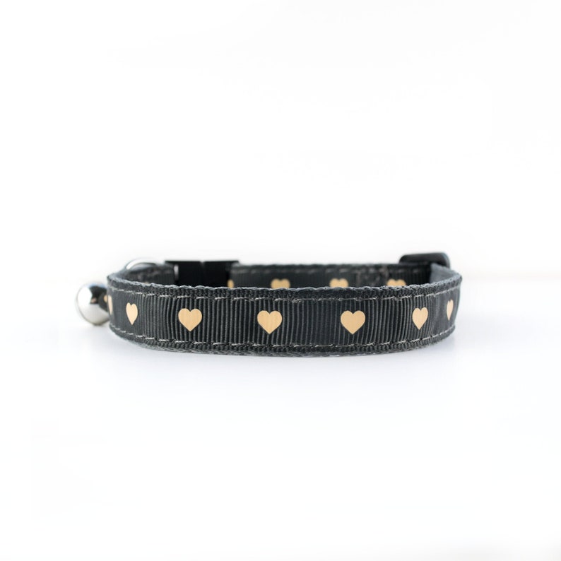May include: A black cat collar with a silver bell and gold heart pattern.
