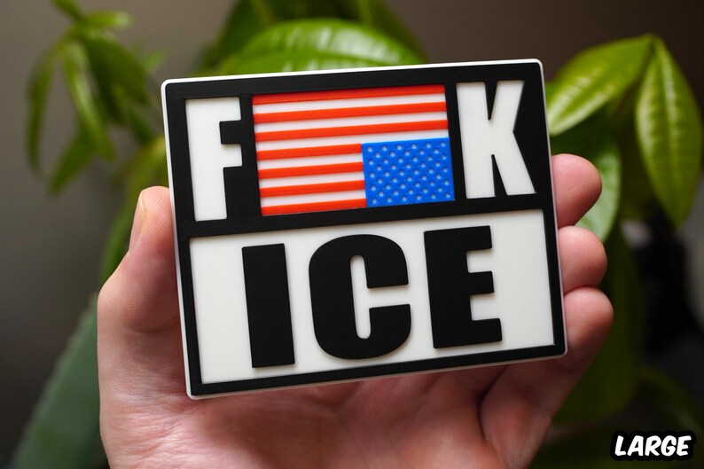 Może przedstawiać: Prostokątna naklejka z napisem "F**K ICE" pogrubionymi czarnymi literami. Litery "F" i "K" są oddzielone fragmentem amerykańskiej flagi. Naklejka jest trzymana w dłoni.