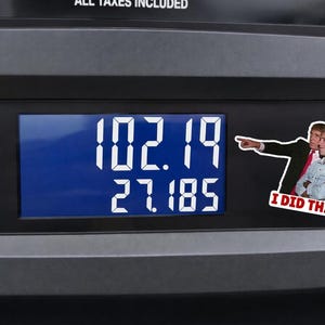 Op de afbeelding: Een benzinepompdisplay toont een prijs van $102,19 en 27,185 gallons. Een sticker met twee mannen en de tekst "I DID THAT!" staat op de pomp.