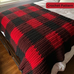 Può includere: Una coperta all'uncinetto fatta a mano con un motivo a quadri di bufalo, con grandi quadrati rossi, neri e rosso scuro. La coperta è drappeggiata su un letto, mostrando la sua superficie strutturata. Il testo "Crochet Pattern" è visibile.