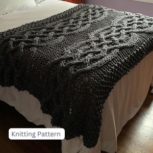 May include: A dark gray knitted blanket with a cable knit design is draped over a bed. The blanket has a textured appearance and a scalloped edge. The text "Knitting Pattern" is in a white box in the lower left corner.