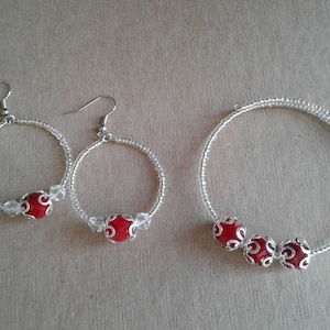 May include: A set of silver hoop earrings and a silver bracelet with red bead accents. The earrings have a single red bead, while the bracelet has three red beads.