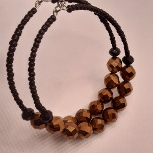 May include: A pair of hoop earrings with black seed beads and gold-toned faceted beads. The earrings are made with a double strand of black seed beads and a single strand of gold-toned faceted beads.