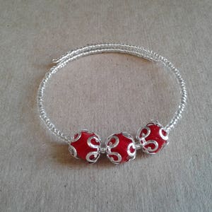 May include: A silver bracelet with three red beads. The beads have a silver filigree design.