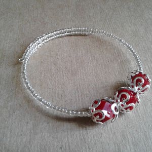 May include: A silver wire bracelet with three red glass beads. The beads are encased in silver filigree.