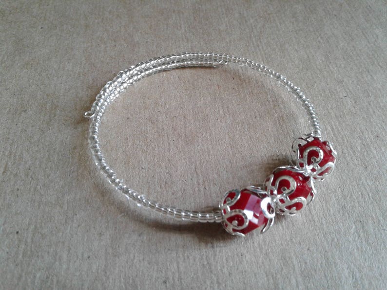 May include: A silver wire bracelet with three red glass beads. The beads are encased in silver filigree.