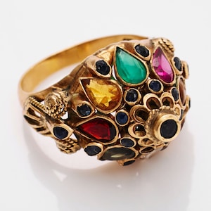 Op de afbeelding: Een gouden ring met een koepelvormige zetting versierd met verschillende gekleurde edelstenen, waaronder smaragd, robijn, saffier en citrien.
