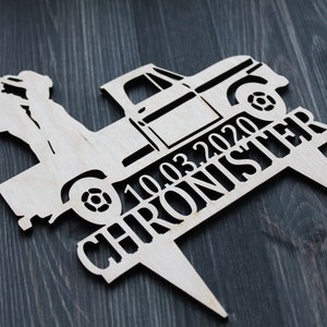 May include: Wooden cake topper featuring a silhouette of a couple standing in the back of a pickup truck. The truck has the date "10.03.2020" and the name "CHRONISTER" written on the side.