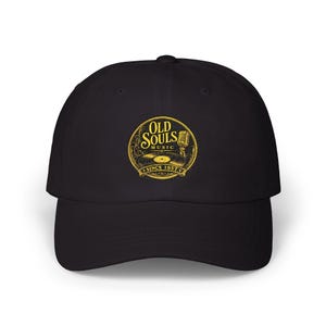 May include: A black baseball cap featuring a circular yellow graphic on the front. The design includes a vintage microphone, a vinyl record, and the text "OLD SOULS MUSIC" with "SINCE 1957" printed below in a decorative, ornate font style.
