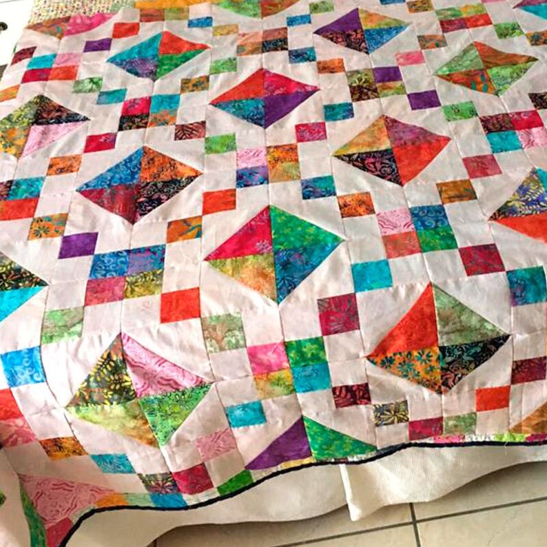 May include: A colorful quilt with a patchwork design featuring a variety of fabrics in shades of red, green, blue, purple, and white. The quilt is made up of squares and triangles, creating a geometric pattern.