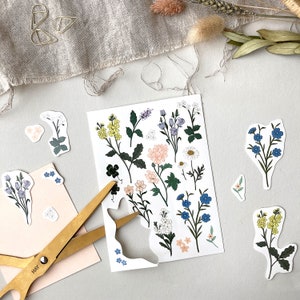 Pu&ograve; includere: Un foglio di adesivi floreali con vari fiori e foglie in tonalit&agrave; di blu, giallo, rosa e verde. Gli adesivi sono su uno sfondo bianco e sono pronti per essere ritagliati e utilizzati per progetti di artigianato.