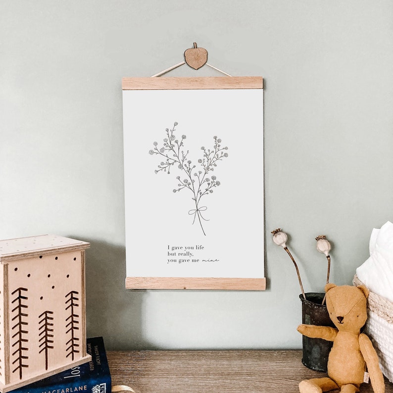 Peut inclure: Une impression en noir et blanc avec un motif floral et le texte "Je t'ai donn&eacute; la vie mais en r&eacute;alit&eacute;, tu m'as donn&eacute; la mienne". L'impression est encadr&eacute;e d'un cadre en bois et accroch&eacute;e &agrave; un mur.