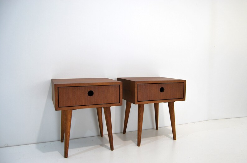 Puede incluir: Dos mesitas de noche de madera con un caj&oacute;n cada una. Las mesitas de noche tienen un acabado marr&oacute;n oscuro y cuatro patas cortas.