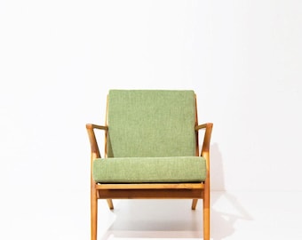 May include: An armchair featuring a light green fabric upholstered seat and backrest, supported by a wooden frame with angled armrests and four straight legs. The chair has a simple, open design with a visible wood grain finish.
