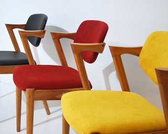 Puede incluir: Tres sillas de madera con tapicería de diferentes colores. Las sillas tienen un diseño angulado único con un respaldo y brazos curvos. Las sillas están tapizadas en tela negra, roja y amarilla.