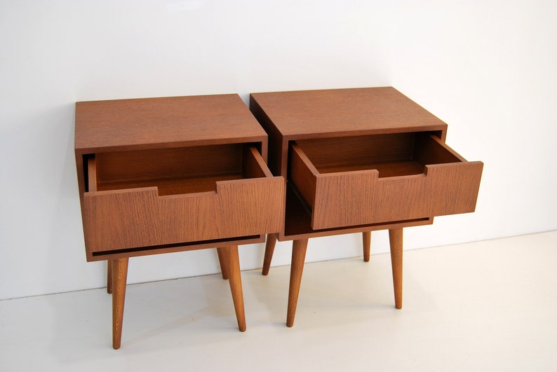 May include: Two wooden nightstands with a single drawer each. The drawer on the right nightstand is open, revealing the empty interior. The nightstands have a mid-century modern design with tapered legs.