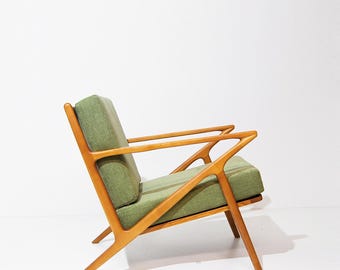 Puede incluir: Un sillón moderno de mediados de siglo con tapicería de tela verde y estructura de madera. El sillón tiene un diseño angulado único con un asiento amplio y cómodo.