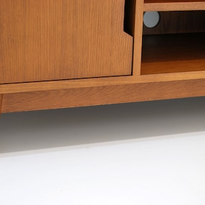 Puede incluir: Consola de medios de madera de estilo moderno de mediados de siglo con acabado marr&oacute;n claro. Cuenta con una puerta de armario, estanter&iacute;as abiertas y patas c&oacute;nicas. El dise&ntilde;o es sencillo y funcional, adecuado para una sala de estar o zona de entretenimiento.