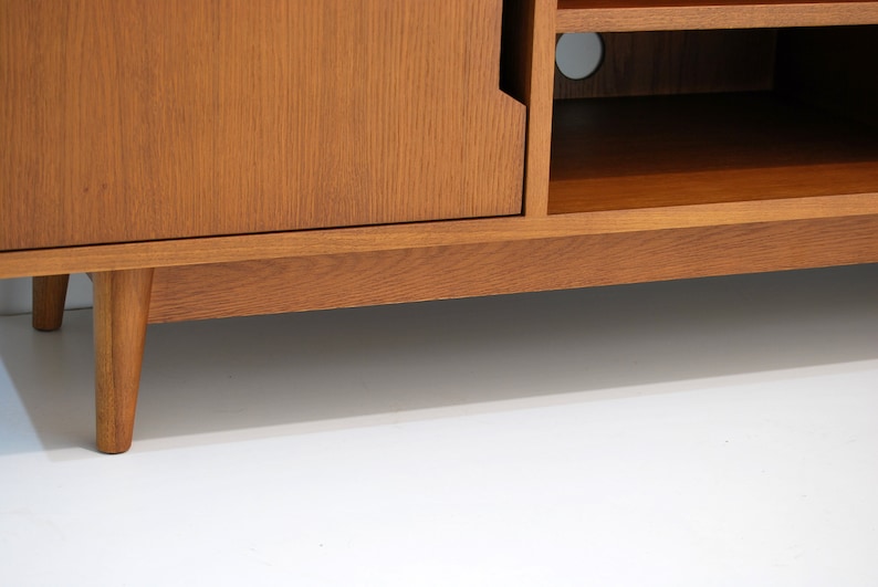 Puede incluir: Consola de medios de madera de estilo moderno de mediados de siglo con acabado marr&oacute;n claro. Cuenta con una puerta de armario, estanter&iacute;as abiertas y patas c&oacute;nicas. El dise&ntilde;o es sencillo y funcional, adecuado para una sala de estar o zona de entretenimiento.
