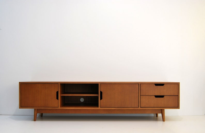 Puede incluir: Una consola de medios de madera de estilo moderno de mediados de siglo. La consola es de color marr&oacute;n c&aacute;lido y presenta dos puertas, dos cajones y un estante abierto. Tiene patas anguladas y un dise&ntilde;o minimalista.