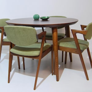 Peut inclure: Un ensemble de salle à manger de style moderne du milieu du siècle, comprenant une table ronde en bois foncé et quatre chaises. Les chaises ont des sièges et des dossiers rembourrés vert olive, avec des cadres en bois.