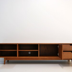 Puede incluir: Consola de medios de madera de estilo moderno de mediados de siglo con estanter&iacute;as abiertas y dos cajones. El mueble es de color marr&oacute;n c&aacute;lido, con las puertas y los cajones abiertos. La consola se apoya en patas anguladas.