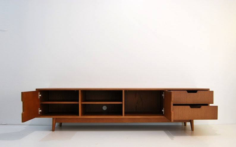 Puede incluir: Consola de medios de madera de estilo moderno de mediados de siglo con estanter&iacute;as abiertas y dos cajones. El mueble es de color marr&oacute;n c&aacute;lido, con las puertas y los cajones abiertos. La consola se apoya en patas anguladas.