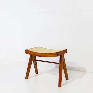 Puede incluir: Un taburete de madera con un asiento curvo de caña trenzada. El taburete tiene un diseño sencillo y moderno de mediados de siglo.