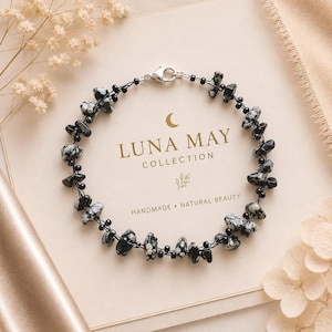 May include: A bracelet featuring black and white speckled stone chips interspersed with small black beads on a thin dark cord. The piece includes a silver-toned lobster claw clasp and is displayed on a card labelled LUNA MAY COLLECTION.