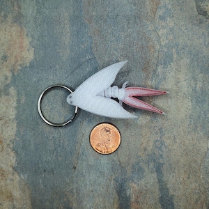 May include: A white and red 3D printed keychain shaped like a mayfly with a silver key ring.