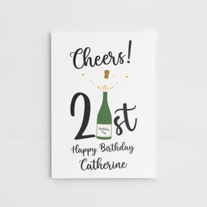Puede incluir: Una tarjeta blanca con texto negro que dice "Cheers! 21st Happy Birthday Catherine". Hay una botella de champ&aacute;n verde con un corcho dorado que sale de la parte superior del n&uacute;mero 21.