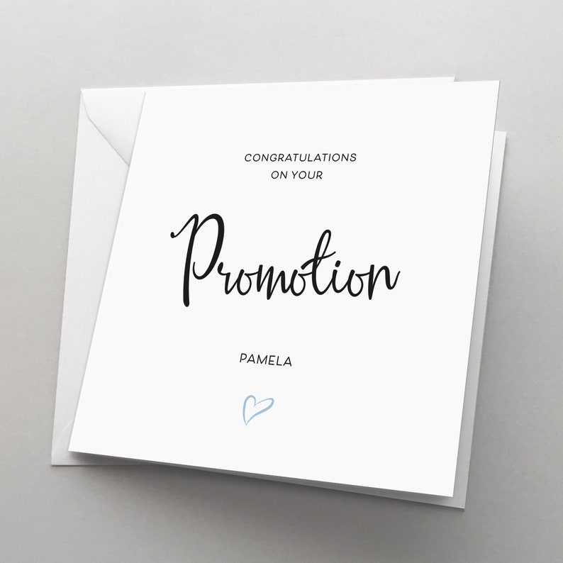 May include: A white card with black text that reads "Congratulations on your Promotion Pamela" with a blue heart symbol below the text.
