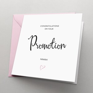 May include: A white card with black text that reads "Congratulations on your Promotion" and "Nimah" with a pink heart below the text.