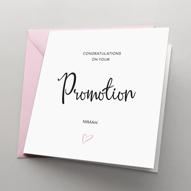 May include: A white card with black text that reads "Congratulations on your Promotion" and "Nimah" with a pink heart below the text.
