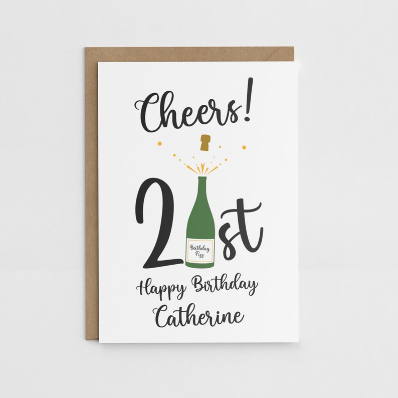 Puede incluir: Una tarjeta blanca con texto negro que dice "Cheers! 21st Happy Birthday Catherine". El n&uacute;mero 21 es grande y el texto est&aacute; en letra cursiva. Hay una botella de champ&aacute;n verde con un corcho dorado que sale de la parte superior del n&uacute;mero 21. La botella tiene una etiqueta que dice "Birthday Fizz".
