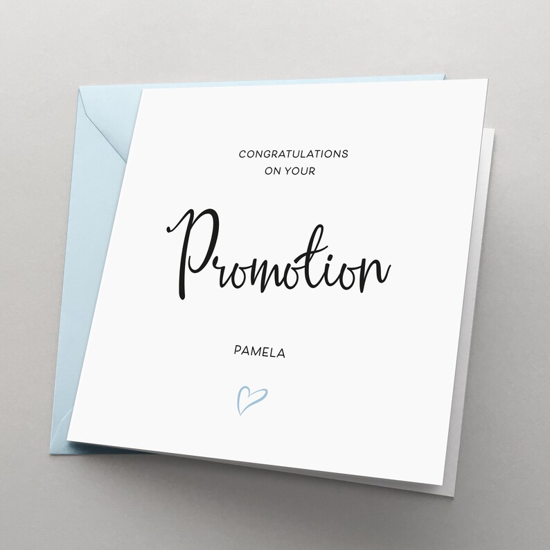 May include: White card with black text that reads "Congratulations on your Promotion Pamela" with a light blue heart drawn in the bottom right corner.