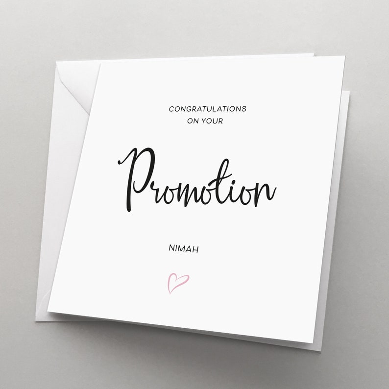 May include: White card with black text that reads "Congratulations on your Promotion" and "Nimah". A pink heart is drawn below the text.