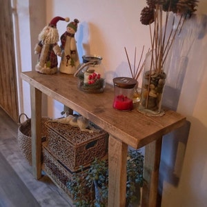 May include: A rustic wooden console table with two shelves. The table is decorated with a snowman and Santa Claus figurine, a glass jar with pine cones and red berries, a glass jar with stones, and a candle in a glass jar.