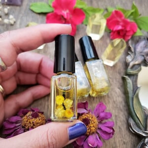 May include: Two small glass bottles with black caps filled with a clear liquid and yellow flowers. The bottles are sitting on a wooden surface.