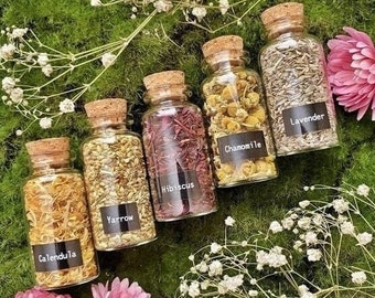 May include: Five small glass jars with cork lids filled with dried herbs and flowers. The jars are labeled with the names of the herbs: Calendula, Yarrow, Hibiscus, Chamomile, and Lavender.