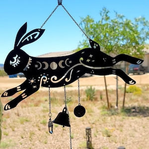 May include: Black metal wind chime featuring a silhouette of a rabbit with moon and star designs. The chime has multiple hanging bells and charms.