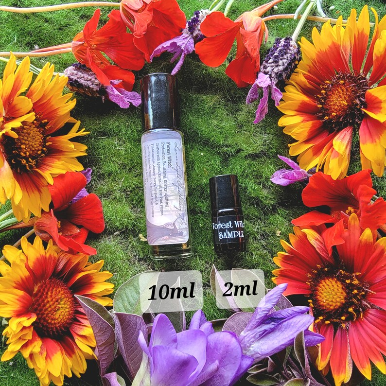 Pu&ograve; includere: Due bottiglie di vetro di olio essenziale con etichette che recitano "Forest Wild" e "Forest Wild Sample". Le bottiglie sono appoggiate su un letto di muschio verde circondato da fiori colorati.